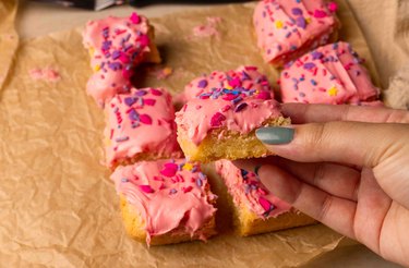 Holding a sugar cookie bars with pink frosting and sprinkles on parchment paper.
