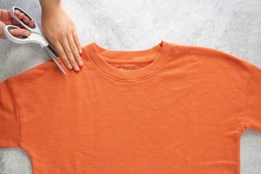 Cutting neckline of orange sweatshirt on a gray background