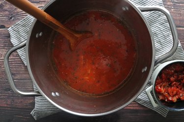 Adding broth and tomatoes to the pot