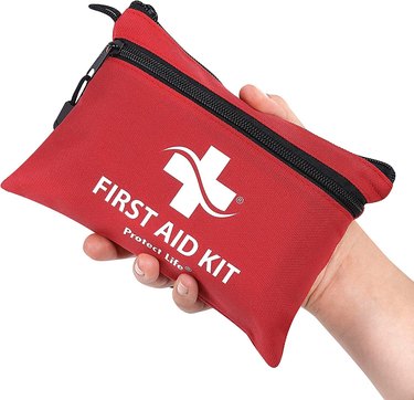 Small, red, zippered first aid kit resting in person's hand.