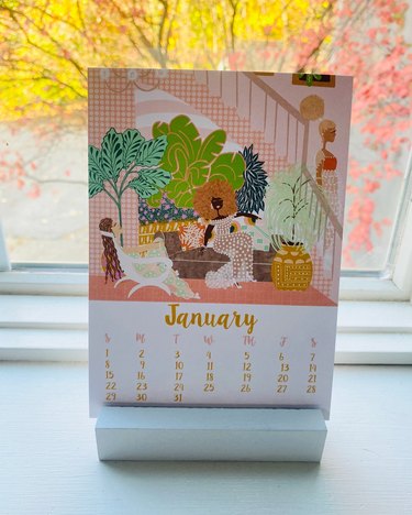 A calendar page for January 2023, featuring vibrant shades of pink, green and blue and a drawing of a dark-skinned woman sitting on a brown couch