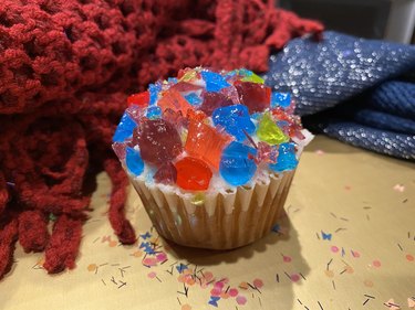 A cupcake with vanilla frosting covered in brightly colored crushed hard candy.
