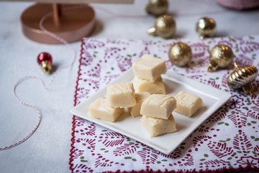 Eggnog white chocolate fudge on a plate surrounded by Christmas ornaments