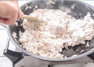 Mixing in cream cheese to beef and onions in a pan for a Cheeseburger Dip recipe