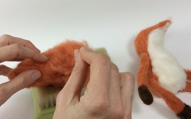 Female hands needle felting an orange mass of wool roving.