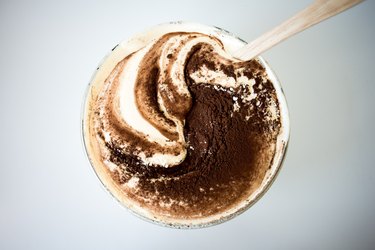 Wooden spoon mixing cocoa powder into batter mixture in a glass bowl.