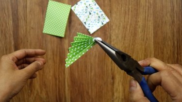 Pinching glued end of paper Christmas tree to secure.