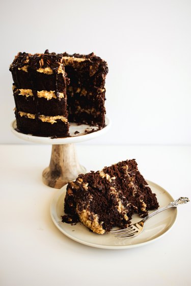 A slice of German chocolate cake on a plate next to the rest of the cake.