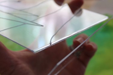 A hand breaking off the back of an acrylic picture frame with a painted design on the front