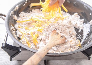 Mixing in shredded cheese to a pan for a Cheeseburger Dip Recipe