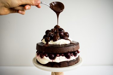 Spoon drizzling chocolate ganache over the top of the Black Forest cake.