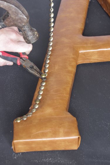 Needle-nose pliers holding nail while hammer taps nail into paper mache center.