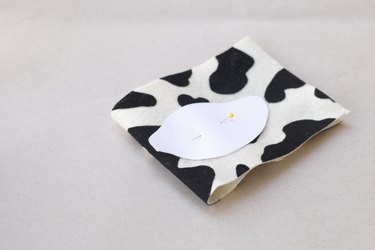 ...A straight pin holds a paper cow ear template to a cut of folded cow print fabric