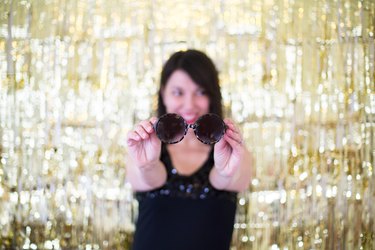 Woman holding out sunglasses in front of a gold backdrop