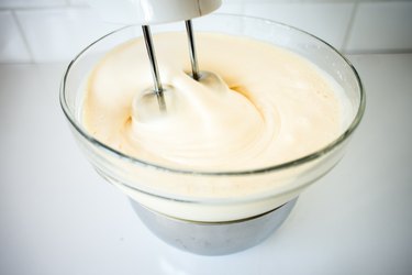 Electric beaters mixing ingredients in a glass bowl.