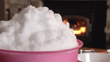 A bowl of fresh snow stands on a table in front of a fireplace.