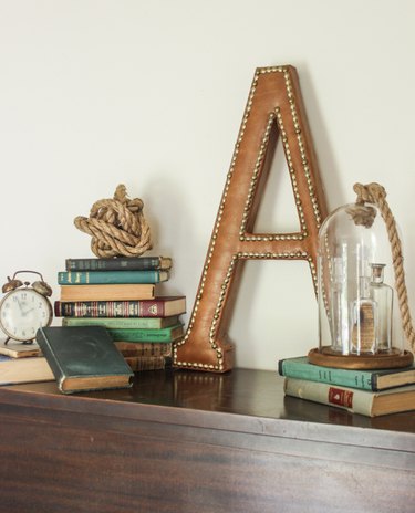 Monogram leather "A"staged with vintage books, vintage clock, rope ball, and glass cloche.