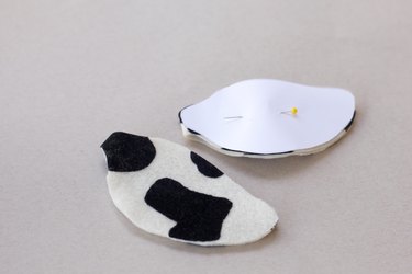 ...One cow ear cut from cow print fabric next to a second one with the paper pattern pinned to it