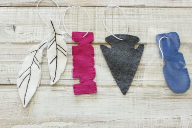 Two feminine shapes: a pair of white feathers, and a pink block-lettered "Mom" cut-out; and two masculine shapes: a dark gray arrowhead and a blue, block-lettered "Dad" cut-out.