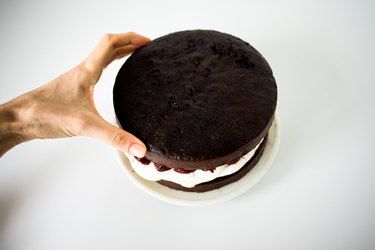 Hand placing the second cake layer over the cream and cherry filling.