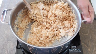 Stirring Rice Krispies into melted marshmallows.