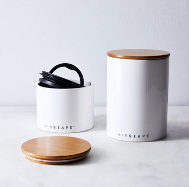 Two airtight white ceramic coffee canisters that say "Airscape" on the bottom and have wooden lids.