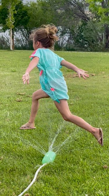 girl jumping through soda bottle sprinkler