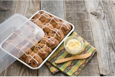 Nordic Ware quarter-sheet pan filled with hot cross buns, shown on weathered wood with lid and a butter dish