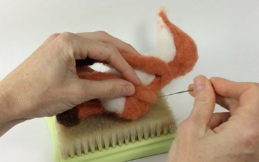 Female hands holding a felting needle while attaching fox limbs