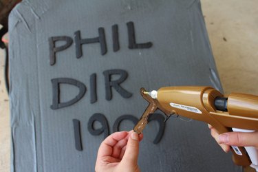 Gluing the letters to the tombstone.