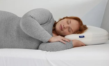 Red haired woman wearing a gray long-sleeved shirt resting her head on a Casper cooling pillow.