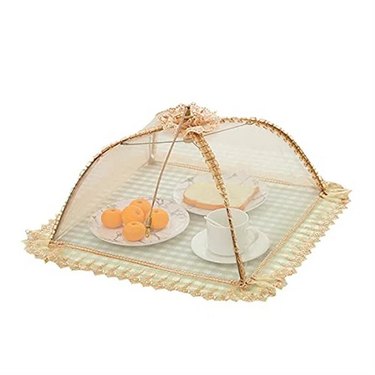 An elegant gold mesh food cover with a floral top and a frilly base