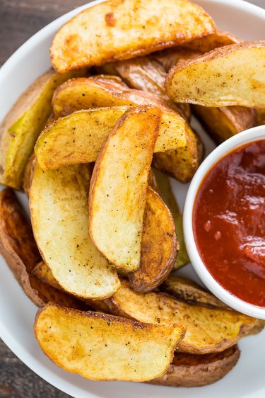 Pan fried potato wedges on a plate with ketchup ready to be served