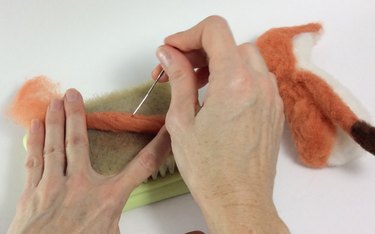 Female hands needle felting a thin limb of wool roving
