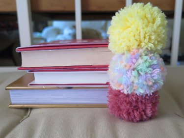 Yarn pompom bookmarks stacked within books