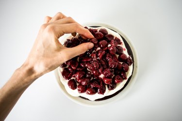 Hand placing some extra cherries on top of the cream and cake layer.