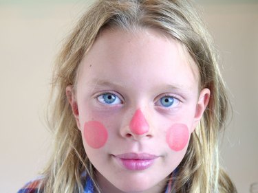 A childs face with peach make up on her cheeks and nose.