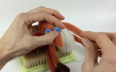 Female hands sewing button eyes onto a needle felted fox.