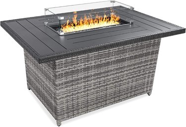 Gray wicker fire pit table (52 inches long) with glass fire protector. There is table space around the flames for placing drinks or snacks.