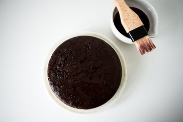 Single cake layer on stand next to a bowl of cherry syrup and a brush for spreading.