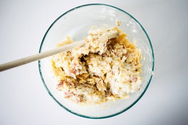 Folding in the cheese to the bowl with the potato mixture.