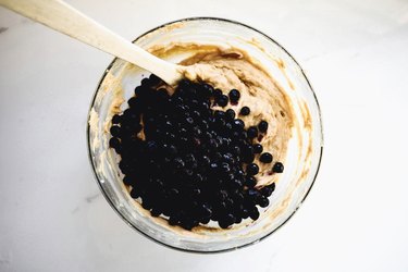 Folding  the blueberries into the batter with a wooden spoon.