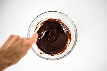 Spoon stirring melted chocolate in a glass bowl.