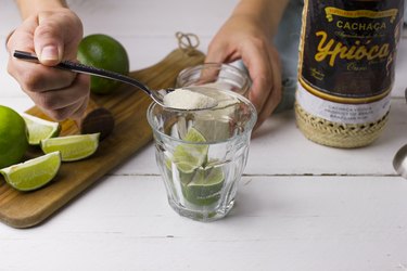 Pouring sugar over limes in a cocktail glass