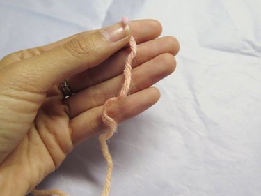 Hand holding a string of yarn, preparing to wrap the yarn around fingers