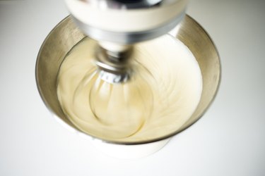 Electric beater whisking cream and sugar in a metal mixing bowl.