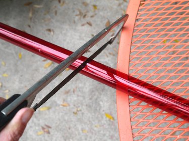 The plastic sleeve on a table with a hand saw cutting off one side.