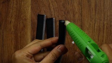 Gluing together three zipper pieces of equal lengths to create a braided zipper bracelet.