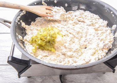 Adding pickle relish to a pan with ingredients for a Cheeseburger Dip recipe