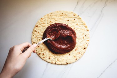 Spreading the pizza sauce generously over the pizza.